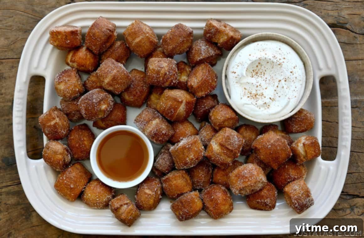 A top-down view of easy Pumpkin Spice Pretzel Bites on a white platter with small bowls containing whipped cream and caramel sauce