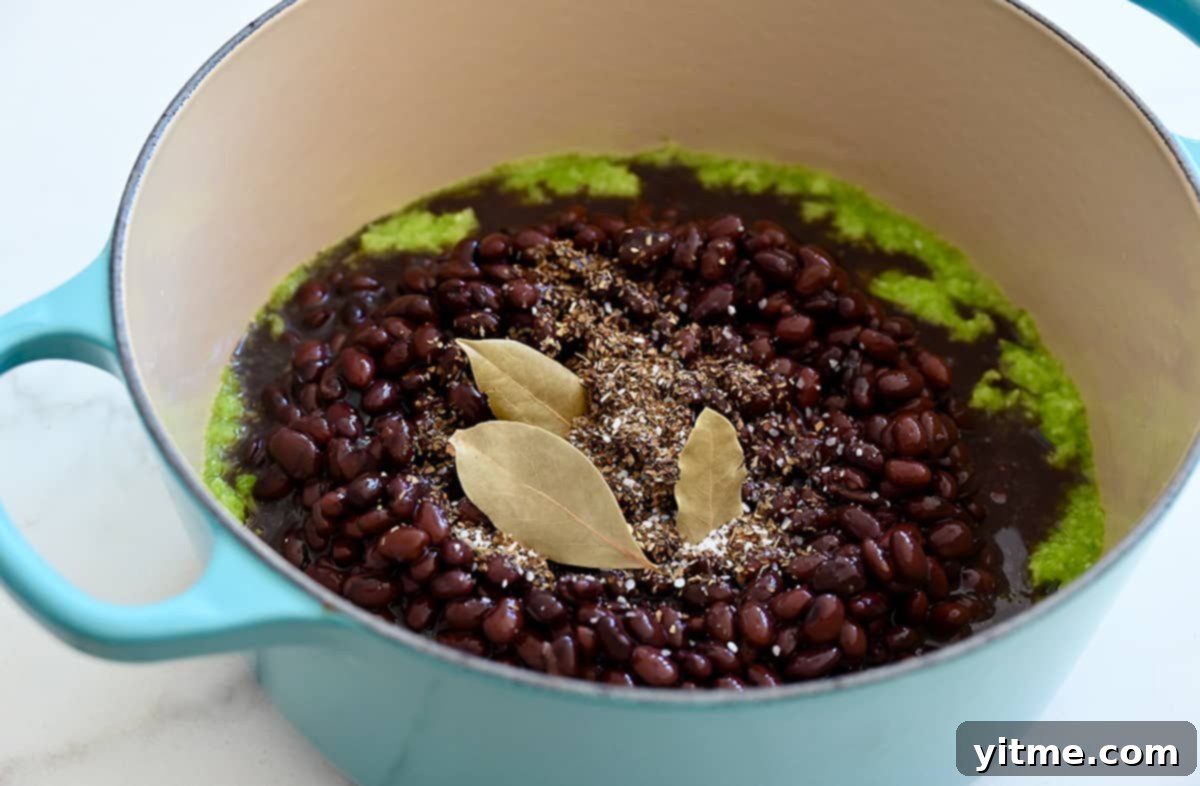 A large pot containing sofrito, black beans, oregano, and bay leaves.