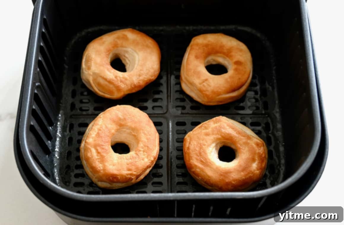 Perfectly golden brown doughnuts and doughnut holes resting in the basket of an air fryer, freshly cooked and ready for toppings.