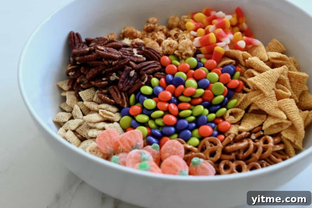 Large white serving bowl with Chex cereal, toasted pecans, caramel corn, candy corn, Bugels, mini pretzels, jelly pumpkin candies, and Halloween-colored M&Ms candies.