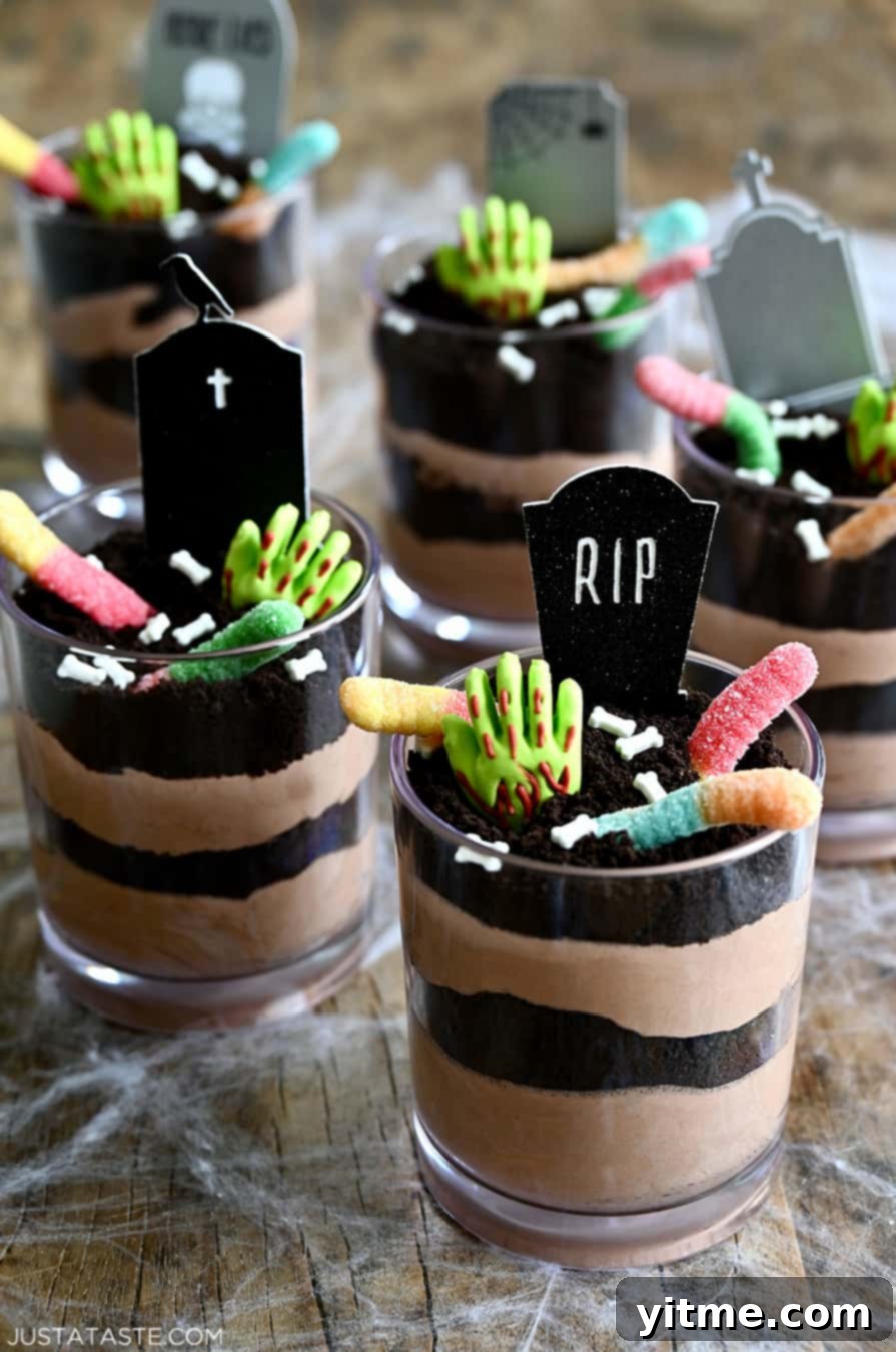 Individual Halloween Dirt Cups decorated with gummy worms, bloody gummy hands, and RIP cake toppers