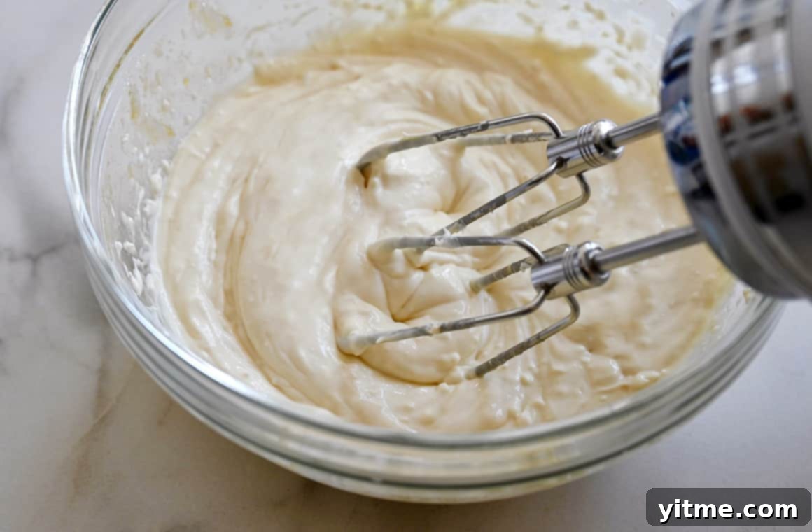 A hand mixer rests on the edge of a clear bowl that contains cream cheese filling