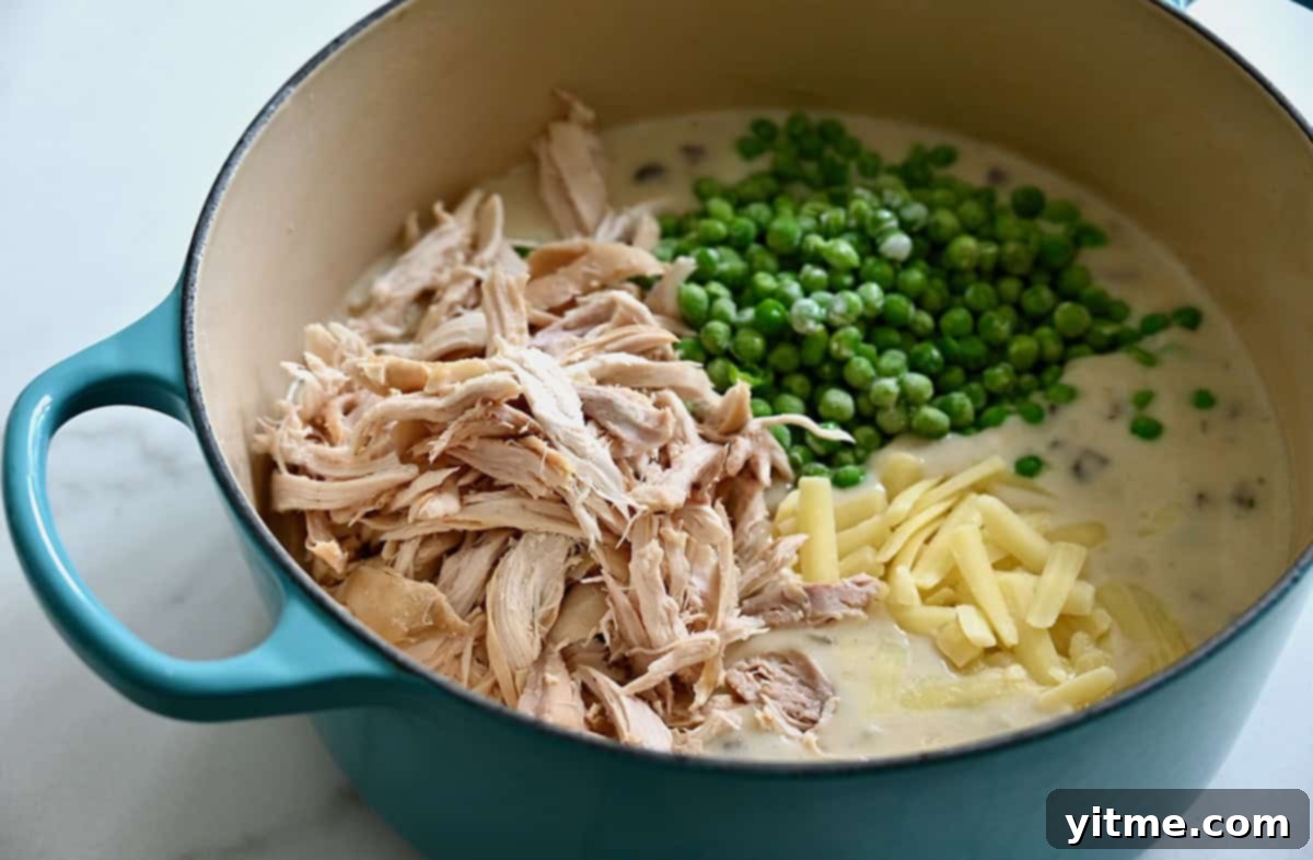 Effortless Turkey Tetrazzini 4 Shredded turkey, bright green peas, and shredded white cheddar cheese being added to a rich, creamy sauce in a Dutch oven for Turkey Tetrazzini.