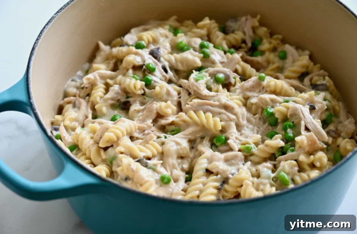 Effortless Turkey Tetrazzini 5 A large stockpot filled with al dente pasta, green peas, and shredded poultry enveloped in a thick, creamy, cheesy sauce, ready for baking.