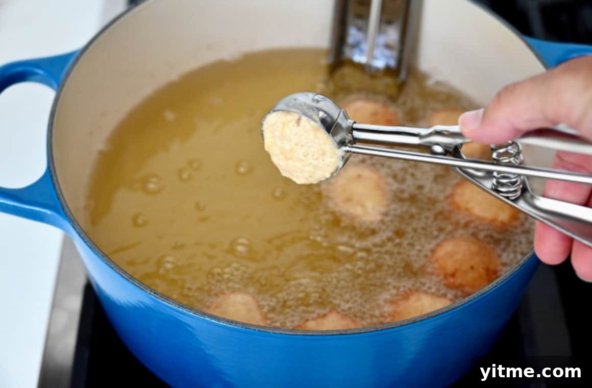 Speedy Banana Fritters 5 A hand holds a small ice cream scoop with banana fritter batter, carefully dropping it into a stockpot of bubbling hot oil.