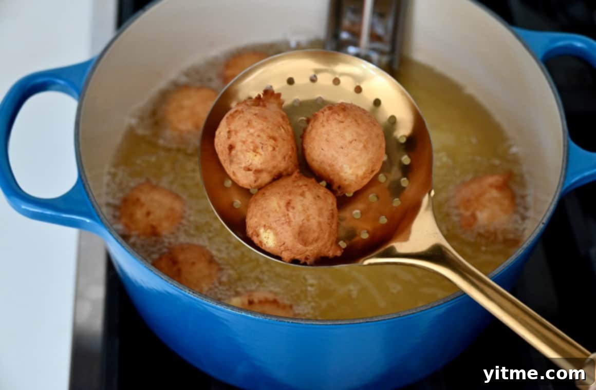 Speedy Banana Fritters 6 A slotted spoon lifts three freshly fried, golden banana fritters from the oil, showing their perfect texture.