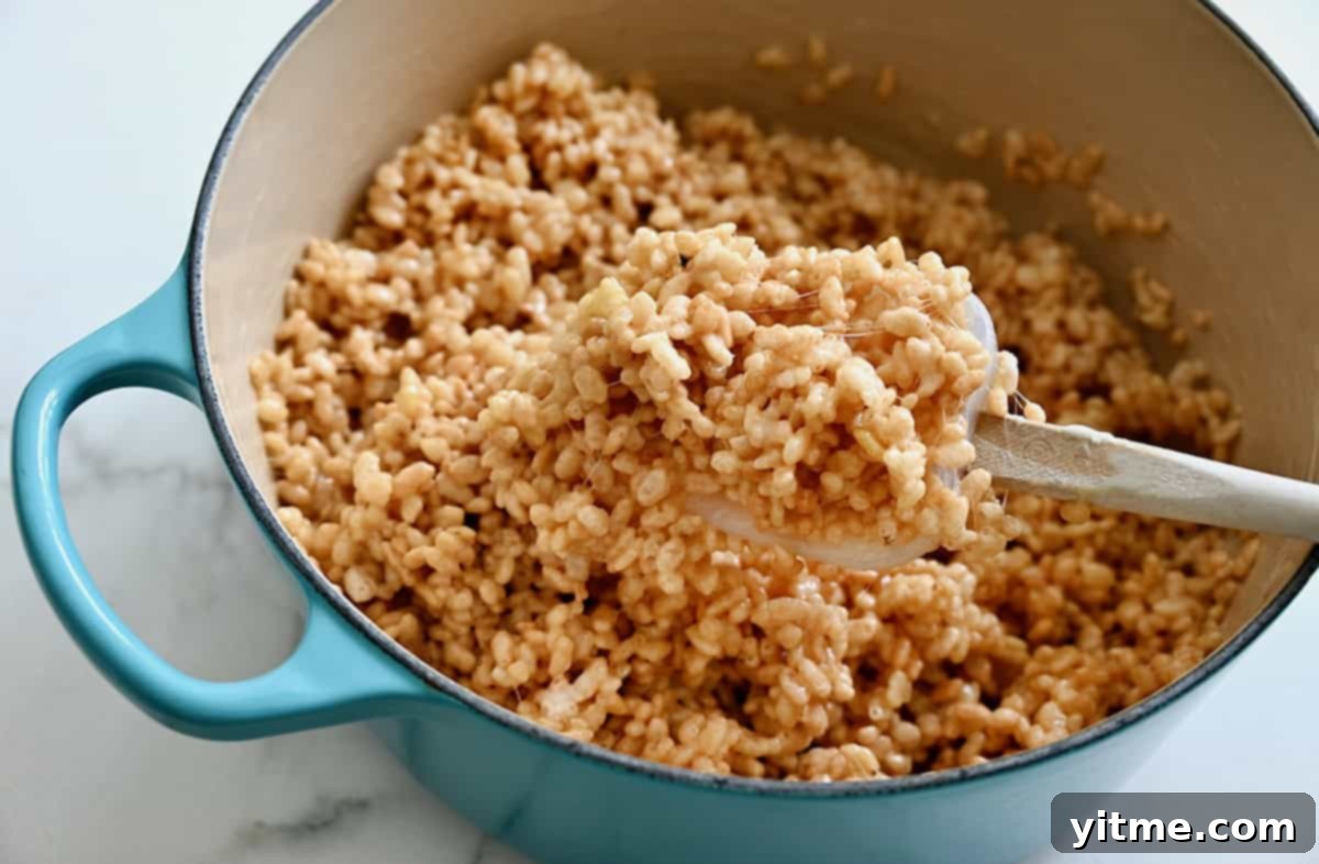 A gooey Rice Krispie-marshmallow mixture being stirred in a blue Dutch oven.