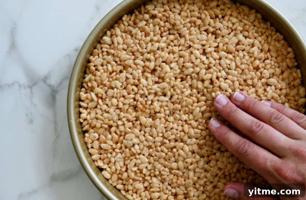A person gently patting marshmallow cereal treats into an even layer in a round cake pan.