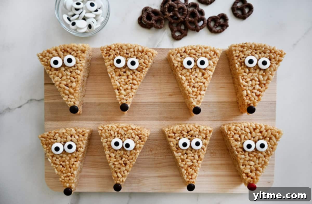 Rice Krispie treat triangles on a wooden cutting board, ready for decorating with candy eyes and M&M noses, with bowls of ingredients nearby.