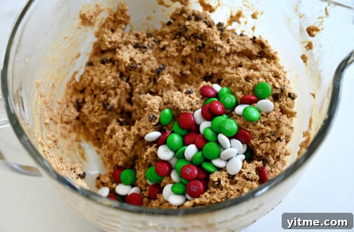 Red, white, and green M&Ms atop a bowl of rich chocolate chip cookie dough, showcasing the festive colors of Christmas monster cookies.
