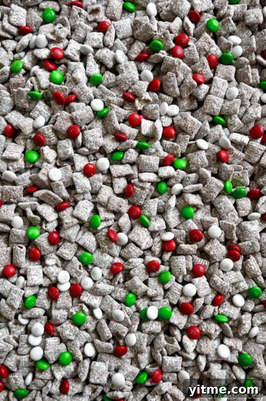 Yuletide Puppy Chow 3 A close-up view of festive holiday Chex Mix, featuring red, green, and white M&Ms mixed throughout the powdered sugar-coated cereal.