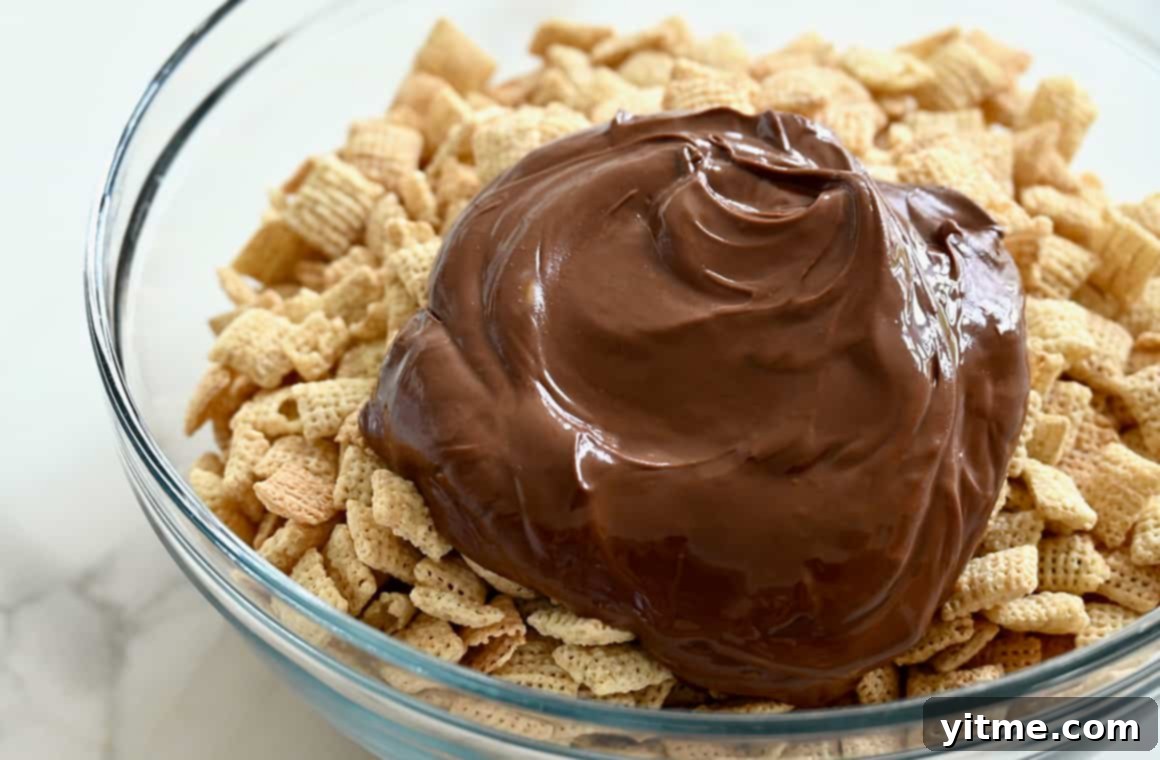 Yuletide Puppy Chow 4 Melted chocolate chips and peanut butter coating Chex Mix cereal in a clear glass mixing bowl, ready to be stirred.