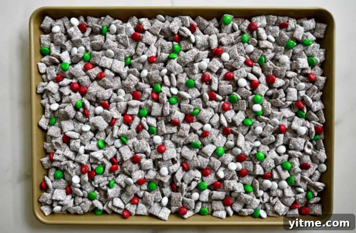 Yuletide Puppy Chow 6 A top-down view of a baking sheet generously topped with holiday muddy buddies, featuring a festive mix of white, red, and green M&Ms.