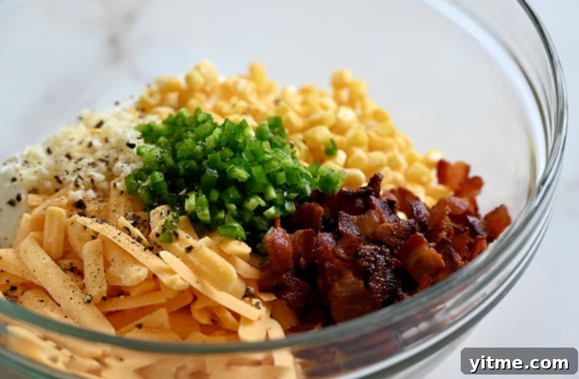 A clear bowl showcasing the vibrant mixture of yellow corn kernels, finely chopped jalapeño, crispy bacon pieces, and shredded sharp cheddar cheese, ready to be combined into a delicious dip