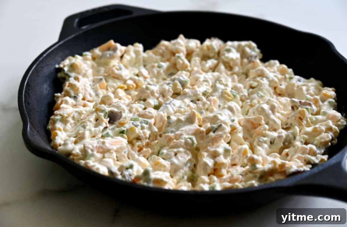 A cast iron skillet filled with the unbaked Jalapeño Corn Dip mixture, showcasing the rich texture and colorful ingredients before baking