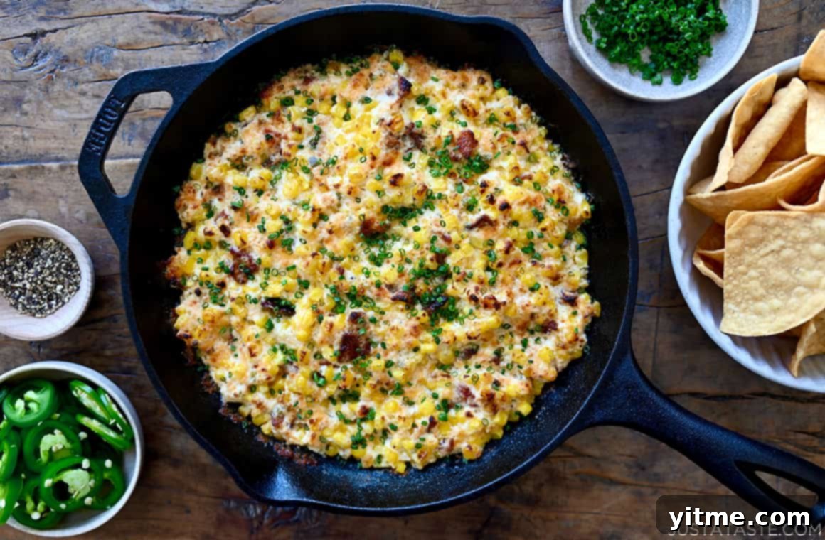 A top-down view of a cast iron skillet brimming with the freshly baked, bubbling hot Jalapeño Corn Dip with Bacon, garnished and ready to be served