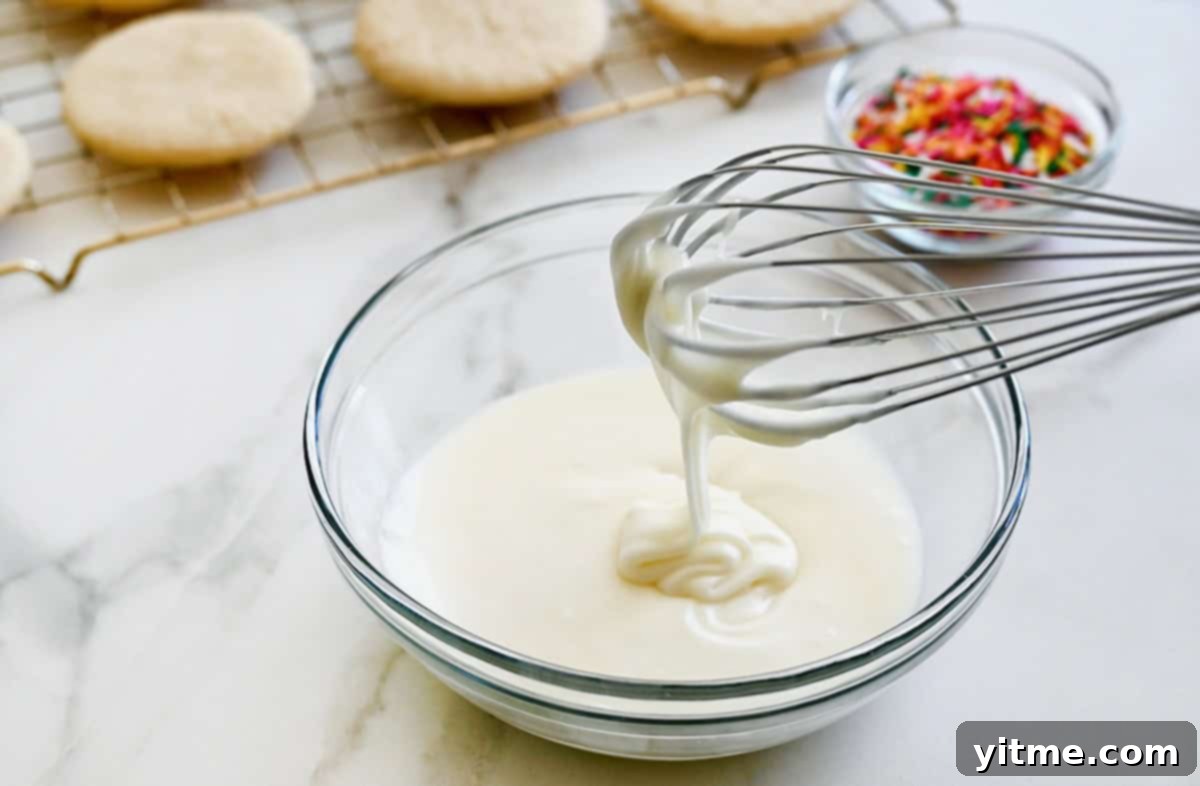 Silky Smooth Sugar Cookie Icing 5 A whisk vigorously mixing easy 3-ingredient icing in a clear bowl, showing its smooth and creamy texture.