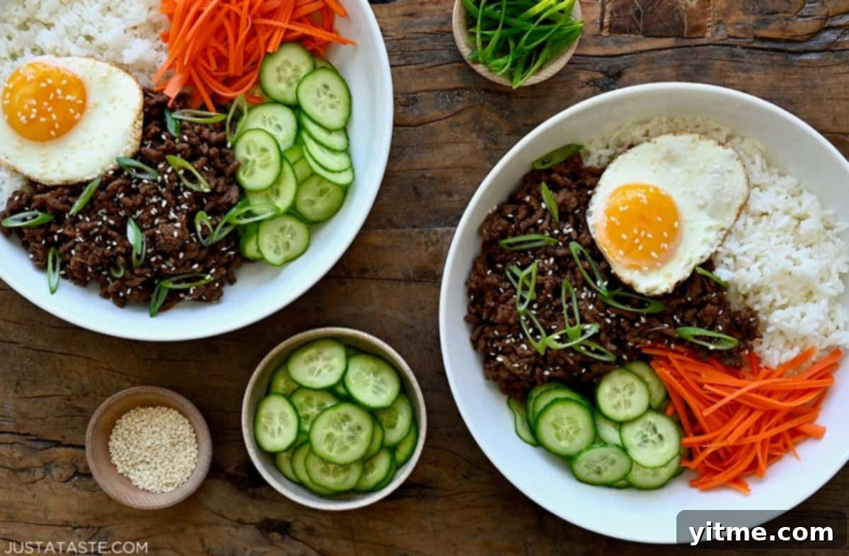 Korean beef bowl with steamed white rice, ground beef in a savory sauce, sliced cucumbers. shredded carrots and sesame seeds.