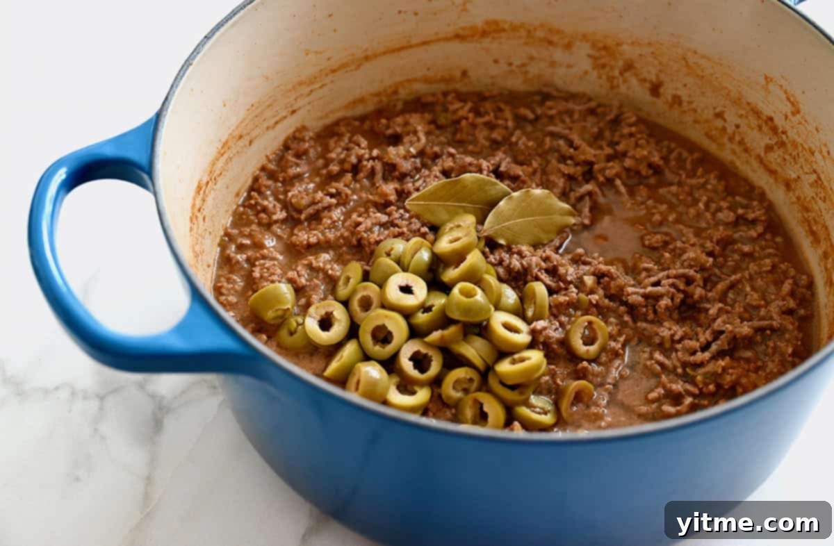 A large stockpot containing ground beef, green olives and two bay leaves.