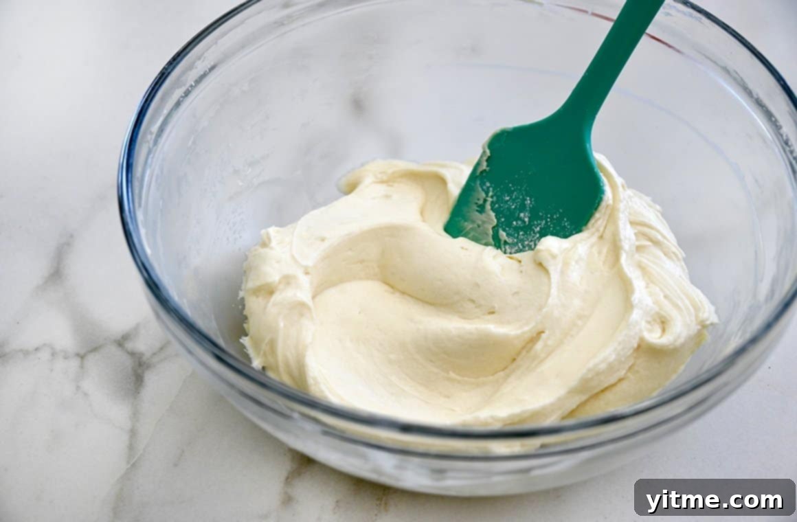 Zesty Carrot Cake Squares with Creamy Frosting 5 Cream cheese frosting in a clear bowl with a teal spatula