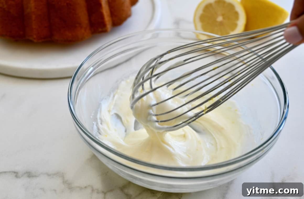 A clear bowl with icing and a wire whisk