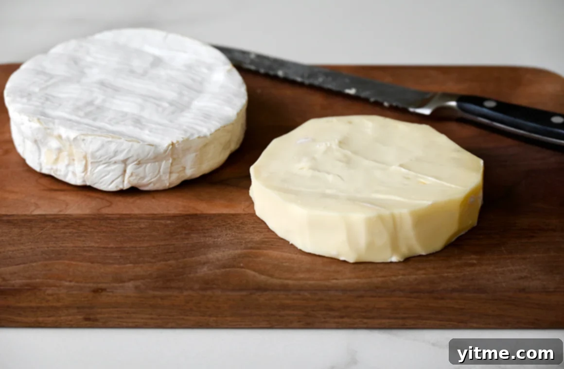 A wood cutting board containing two wheels of Brie cheese and a serrated knife
