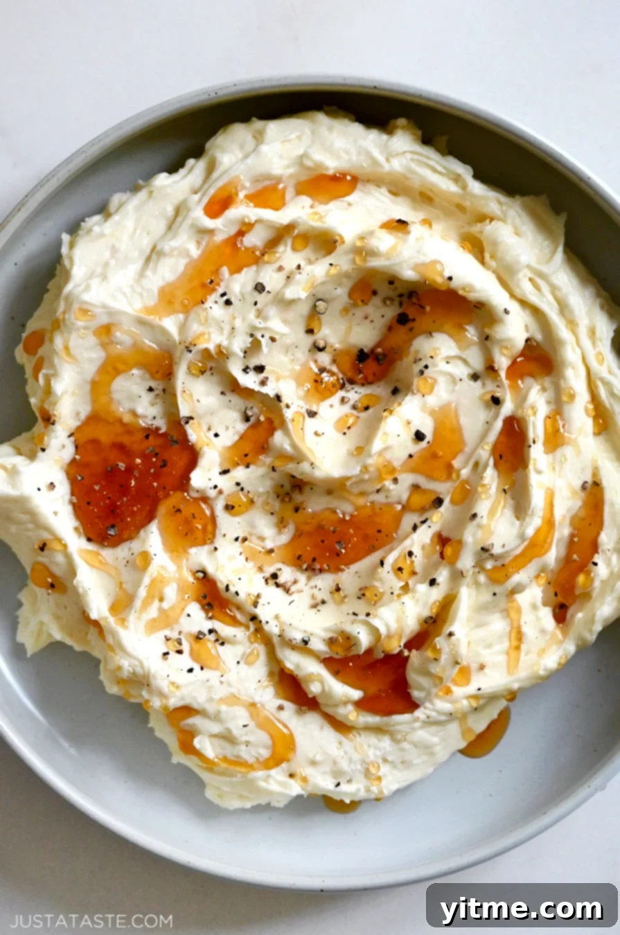A top-down close-up view of a grey bowl containing whipped Brie cheese topped with honey and black pepper