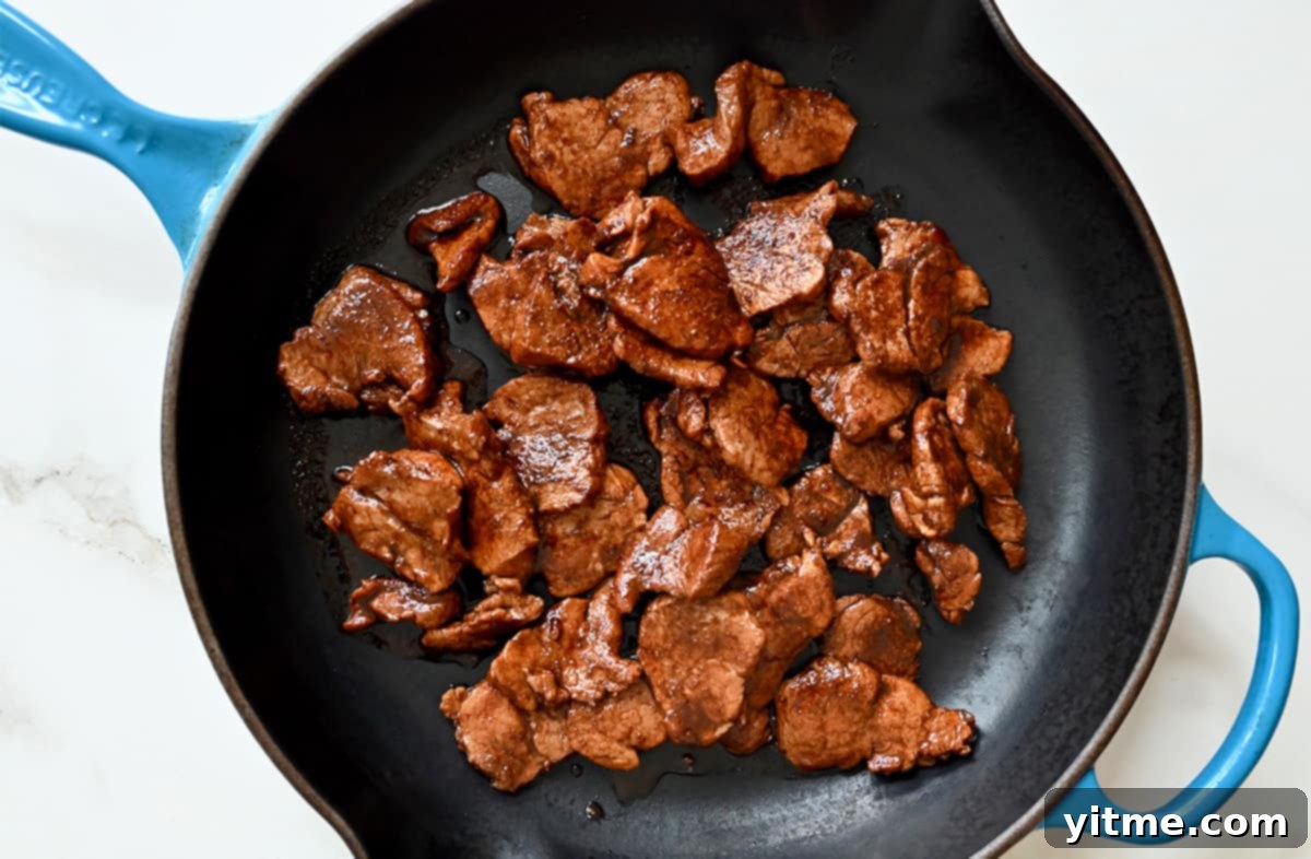 A top-down view of caramelized pork pieces in a large skillet.