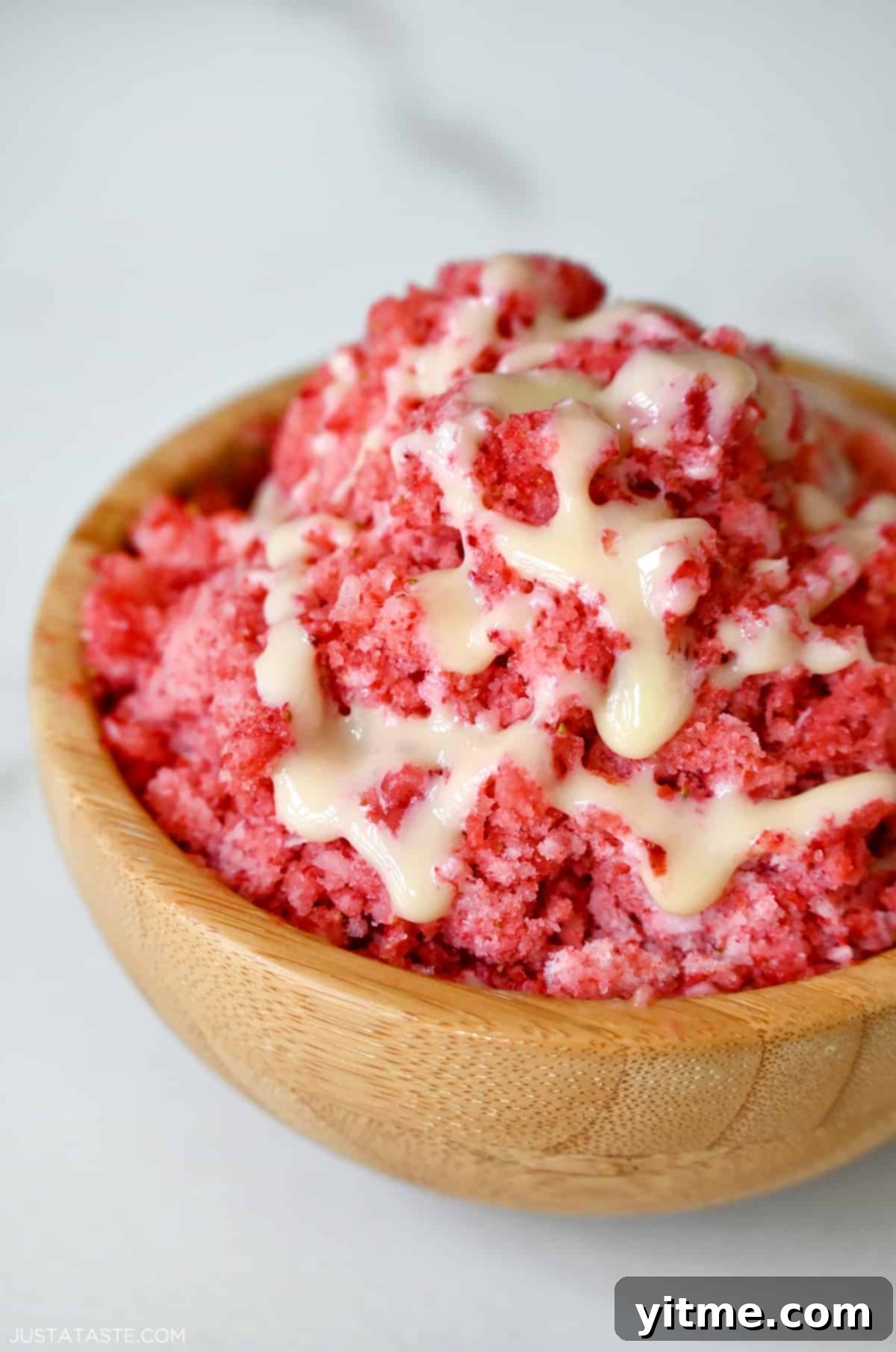 Strawberry shaved ice with sweetened condensed milk drizzled on top in a wooden bowl