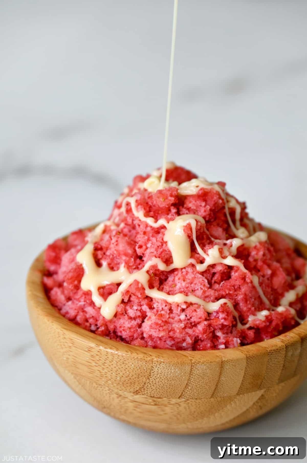 A wood bowl containing strawberry shaved ice with a drizzle of sweetened condensed milk