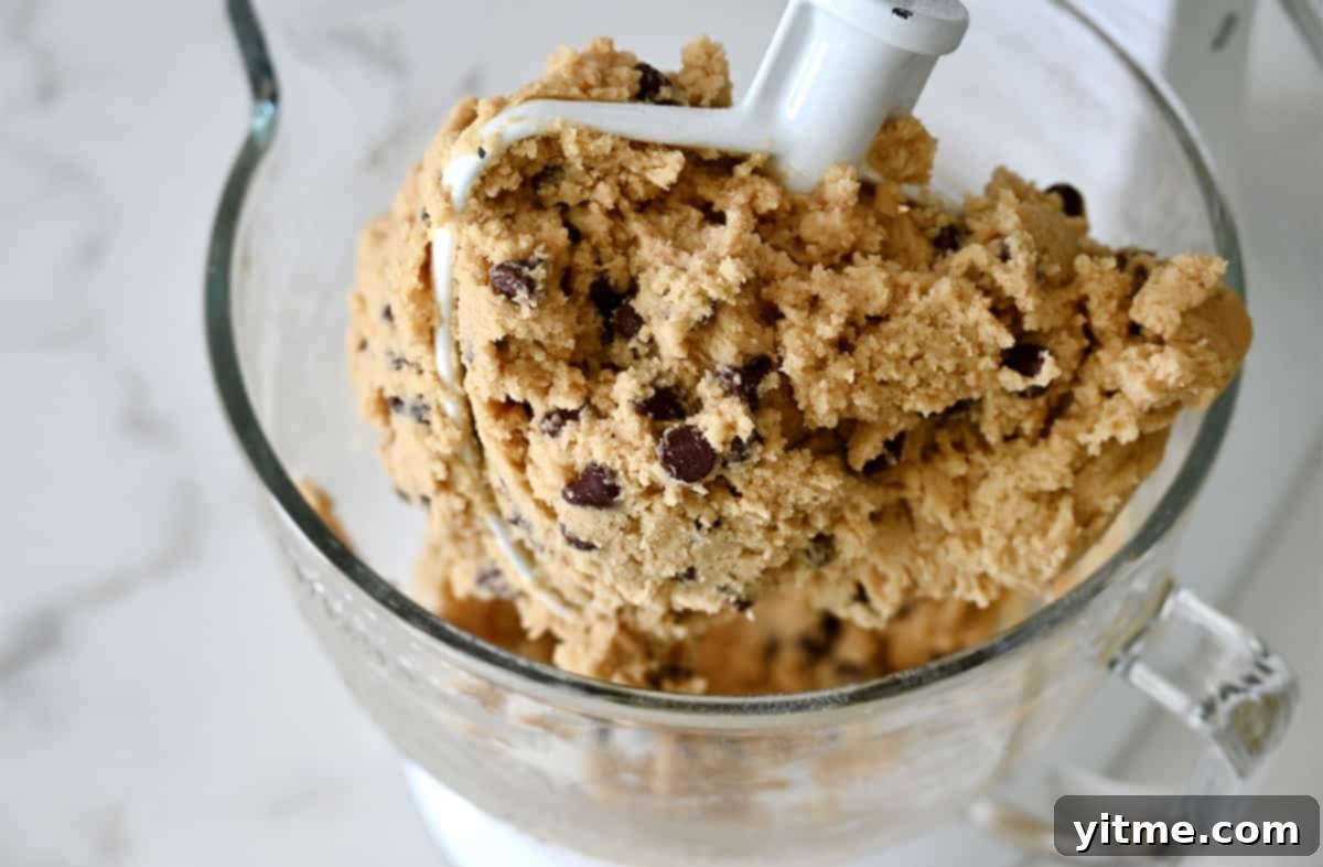 Ruby Velvet Brownie Cookies 4 A large stand mixer bowl with the paddle attachment, filled with creamy, golden-brown cookie dough batter, showing its readiness for the next steps in the brookie recipe preparation.