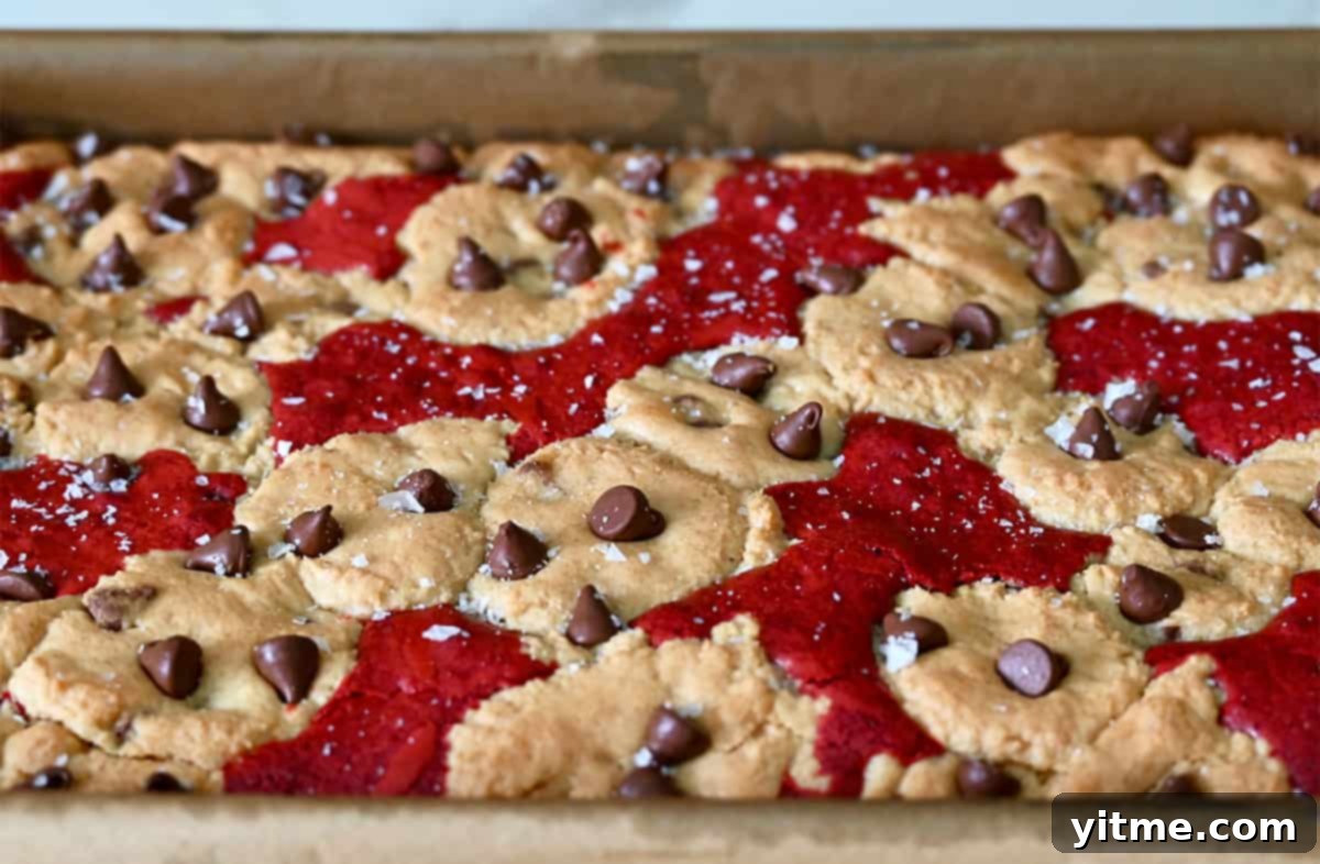 Ruby Velvet Brownie Cookies 8 A pan of perfectly baked red velvet brookies, still warm from the oven, showcasing their beautiful red and brown layers with visible chocolate chips throughout, ready to be cooled and sliced.