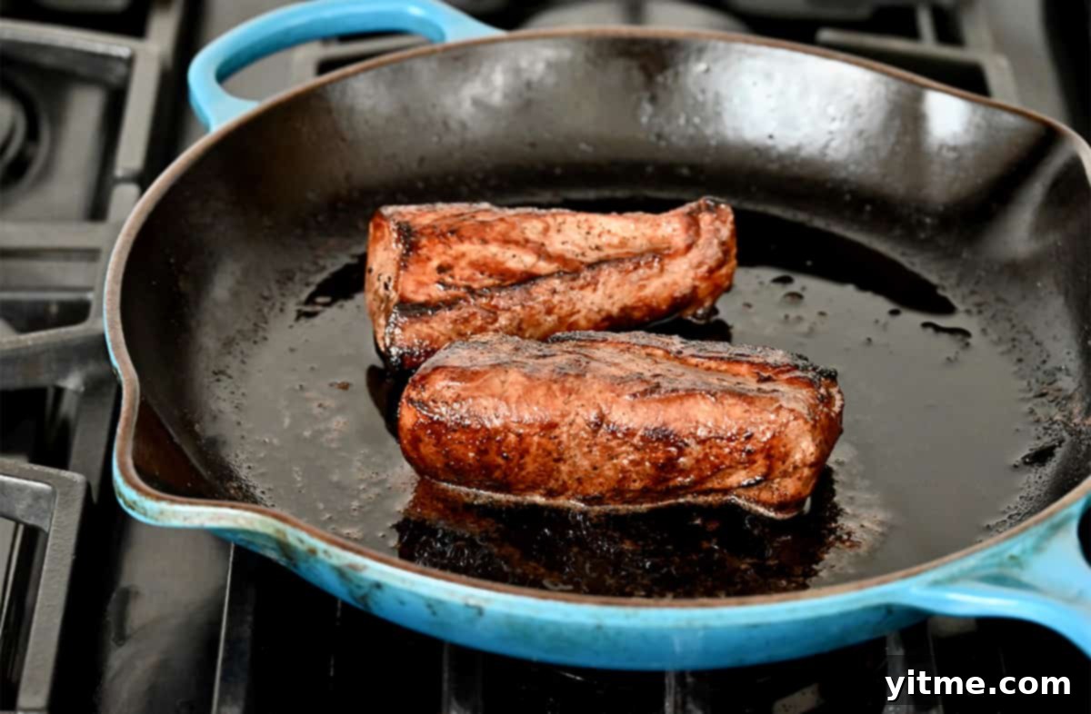 Two seared pork tenderloins in a large cast-iron skillet.