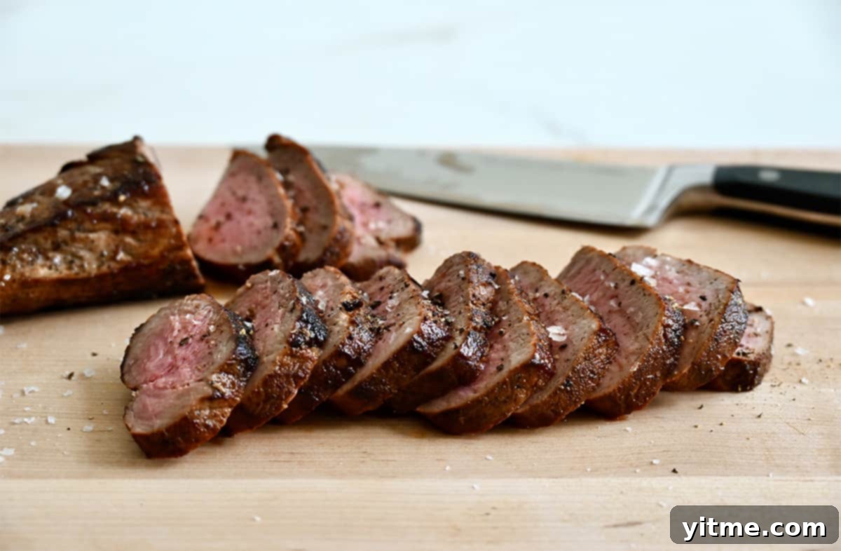 Sliced pork tenderloin on a wood cutting board with a sharp knife.
