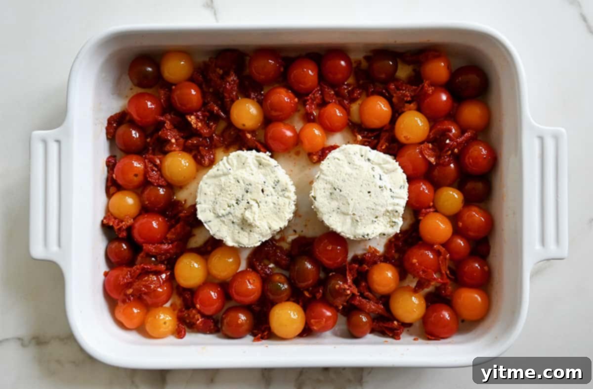 A top-down view of a white baking dish with two Boursin cheese rounds surrounded by cherry tomatoes and sun-dried tomatoes.