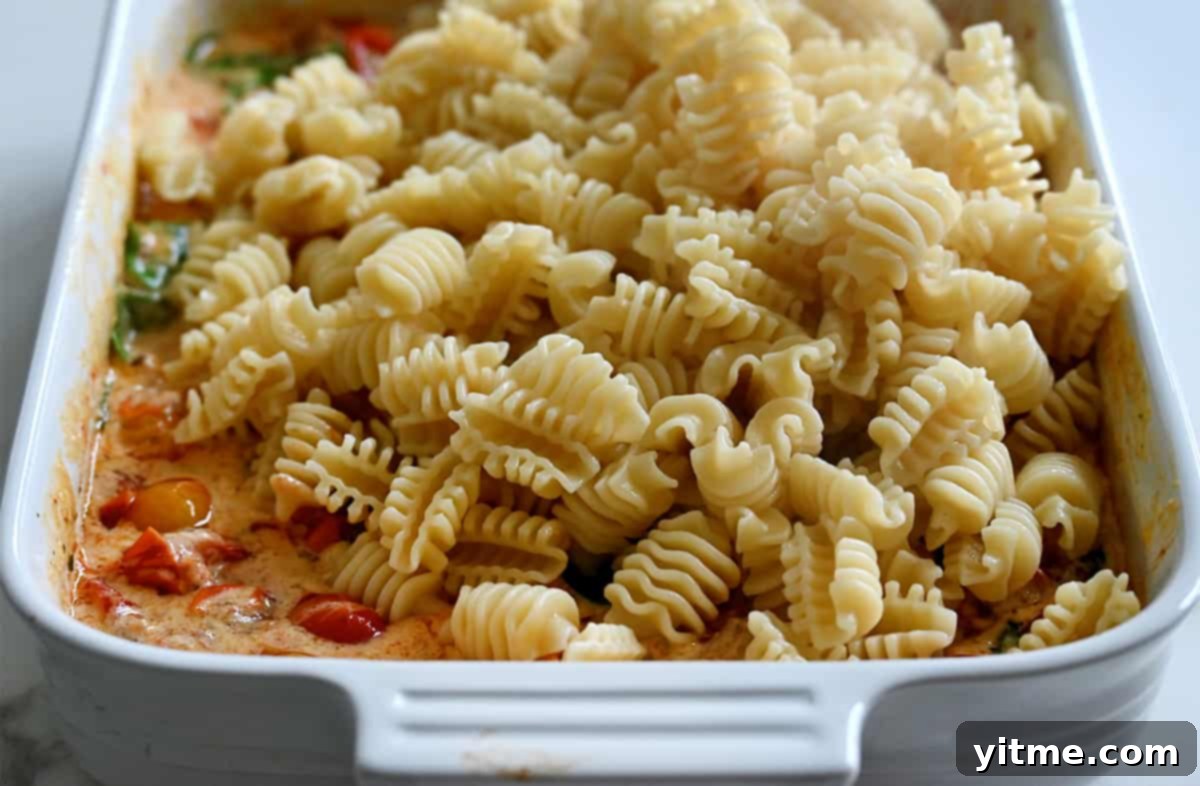 Radiatori noodles over roasted tomatoes mixed with cheese in a white baking dish.