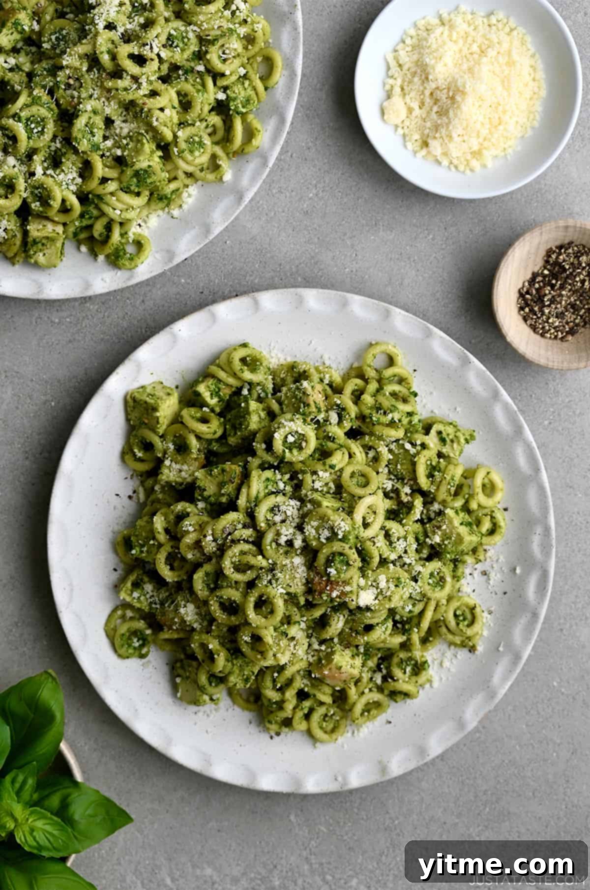 A top-down view of a plate topped with pesto pasta with chicken garnished with Parmesan cheese, ready to be served.