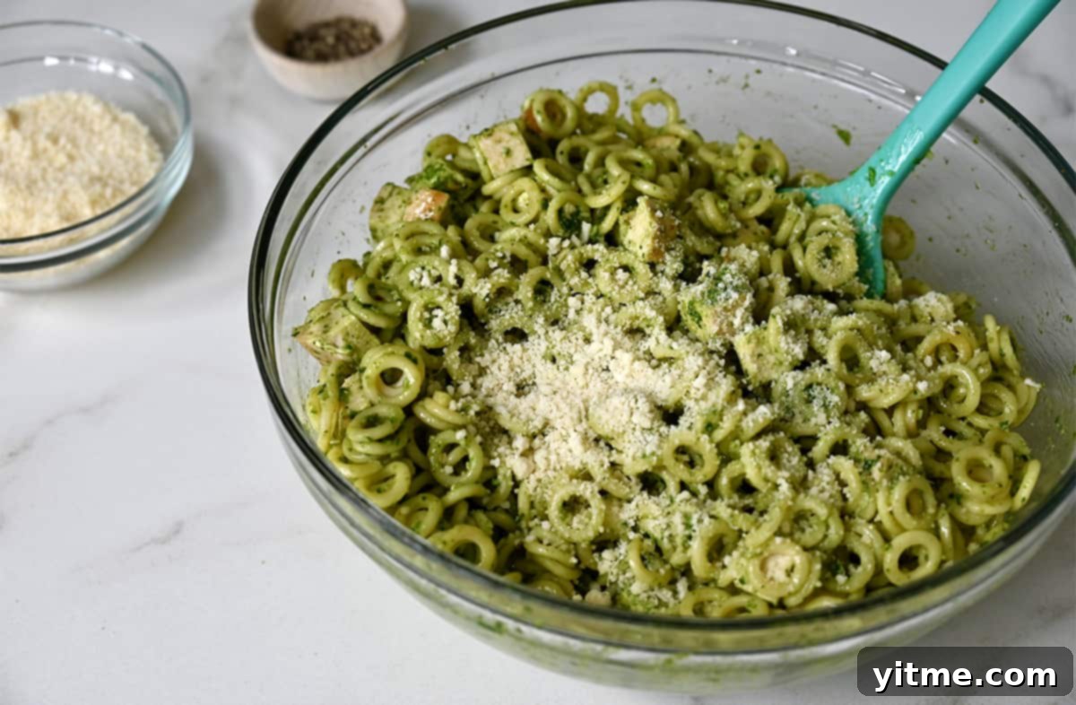 Ring-shaped pasta tossed with vibrant basil pesto in a clear bowl, garnished with freshly grated Parmesan cheese.