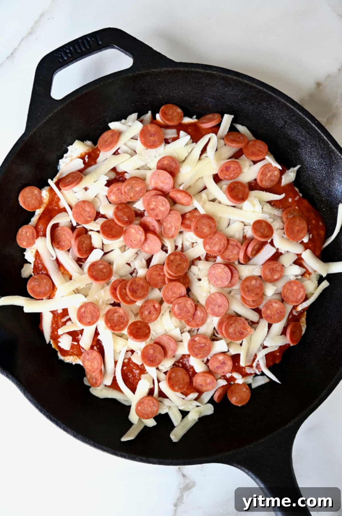 Unbaked pepperoni pizza dip in a cast iron skillet topped with shredded mozzarella cheese.