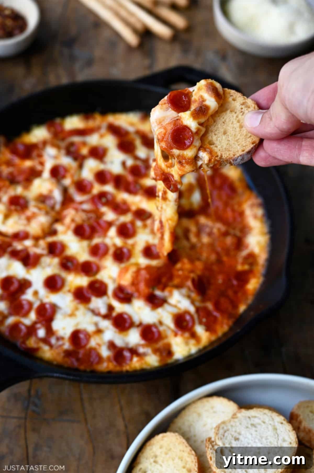 A hand holds a toast that's been dipped into cheesy pizza dip with pepperoni.