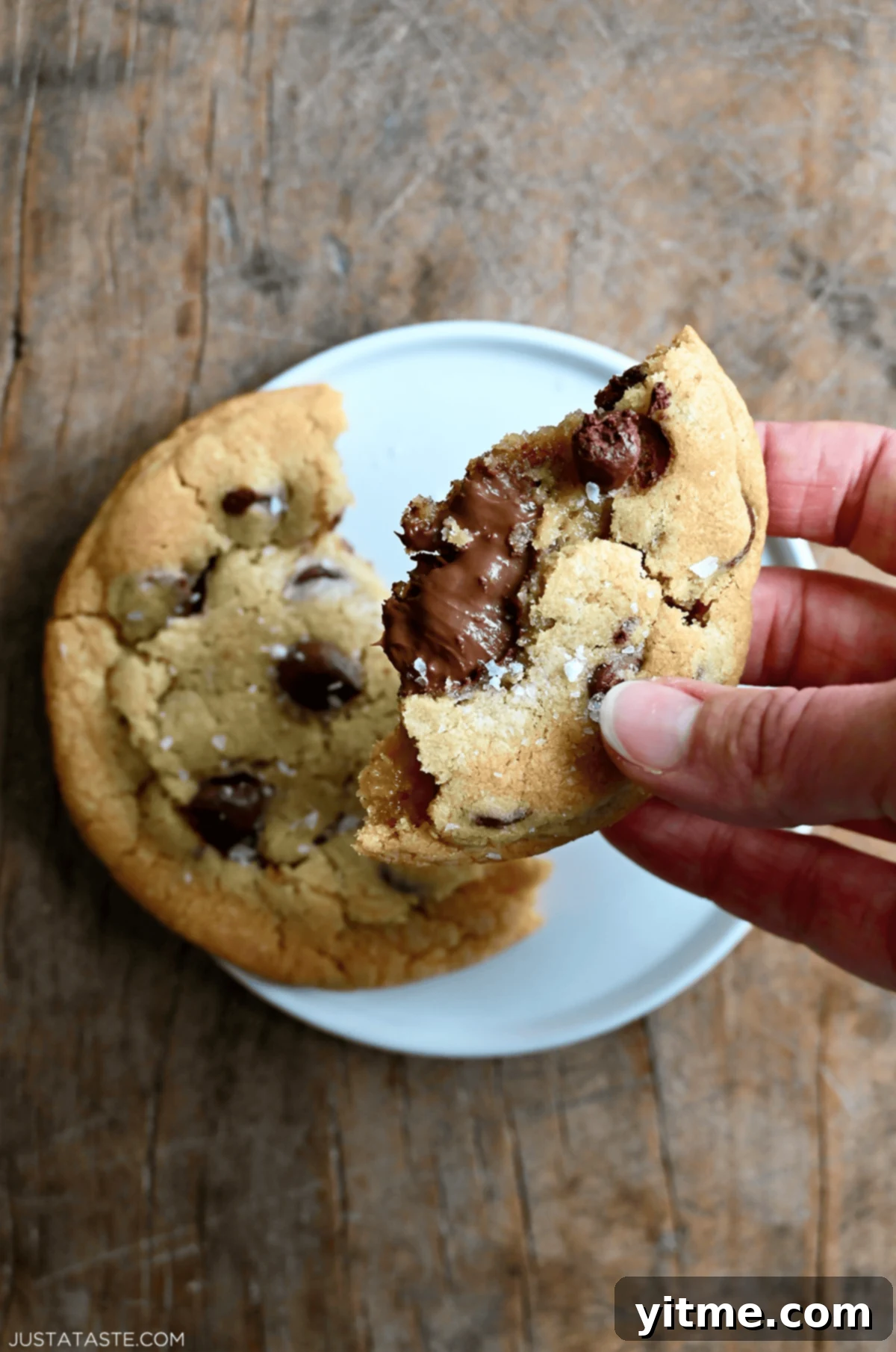 A hand holding a chocolate chip cookie half, with warm Nutella oozing out.