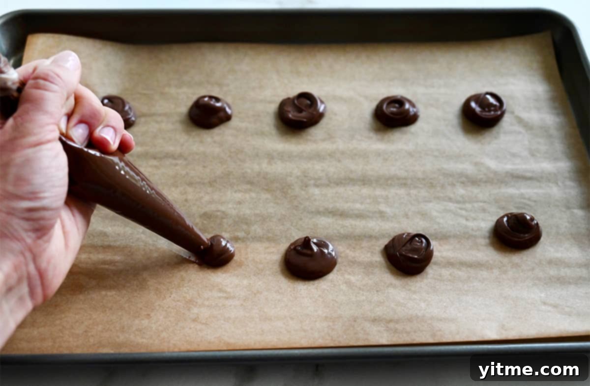 A hand piping mounds of Nutella onto a baking sheet lined with parchment paper.