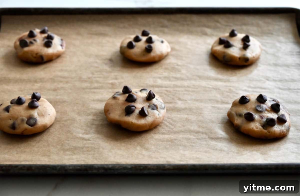 Cookie dough balls stuffed with chocolate chips on a baking sheet lined with parchment paper.
