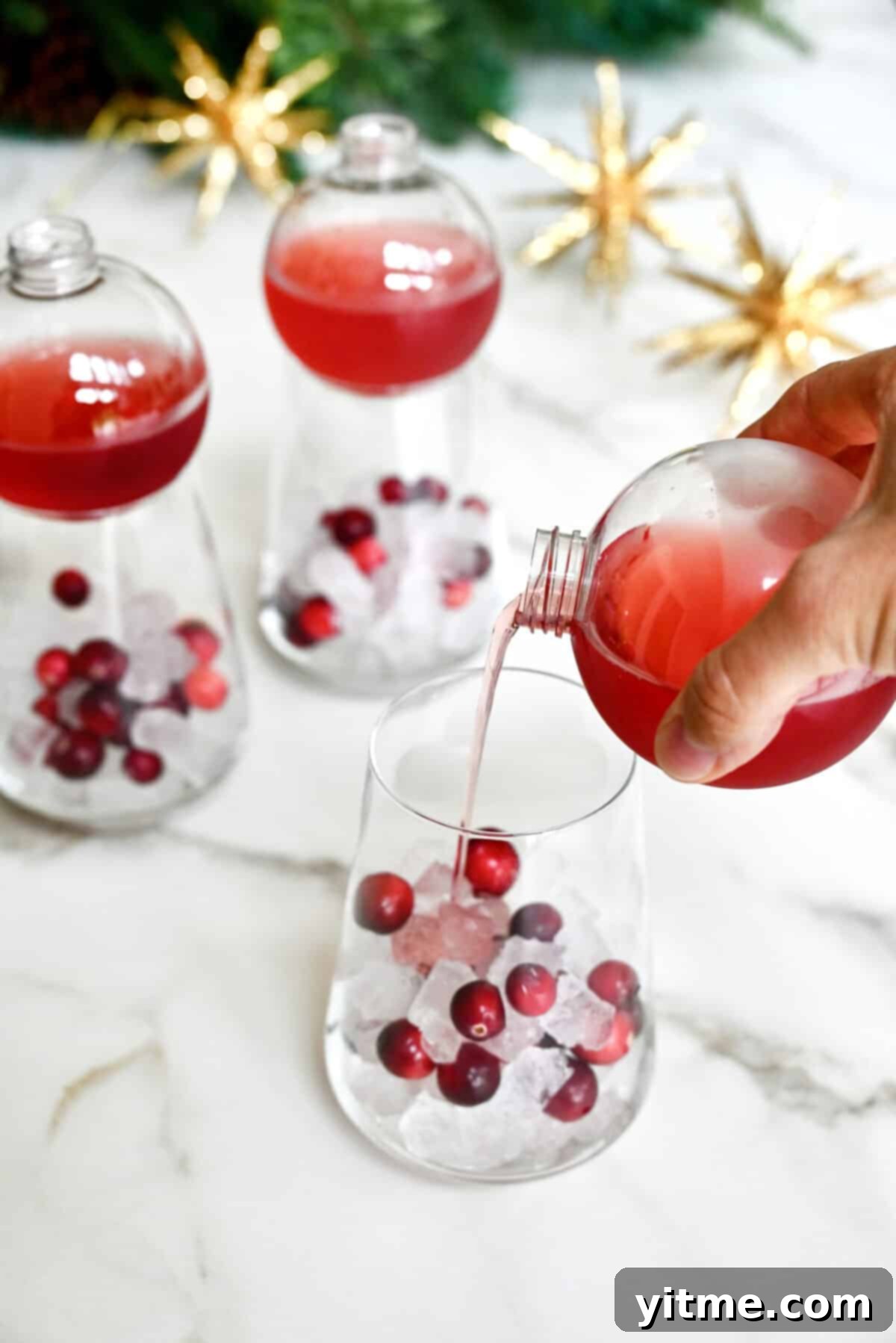 Pouring Christmas Margarita mix into a glass with ice and cranberries