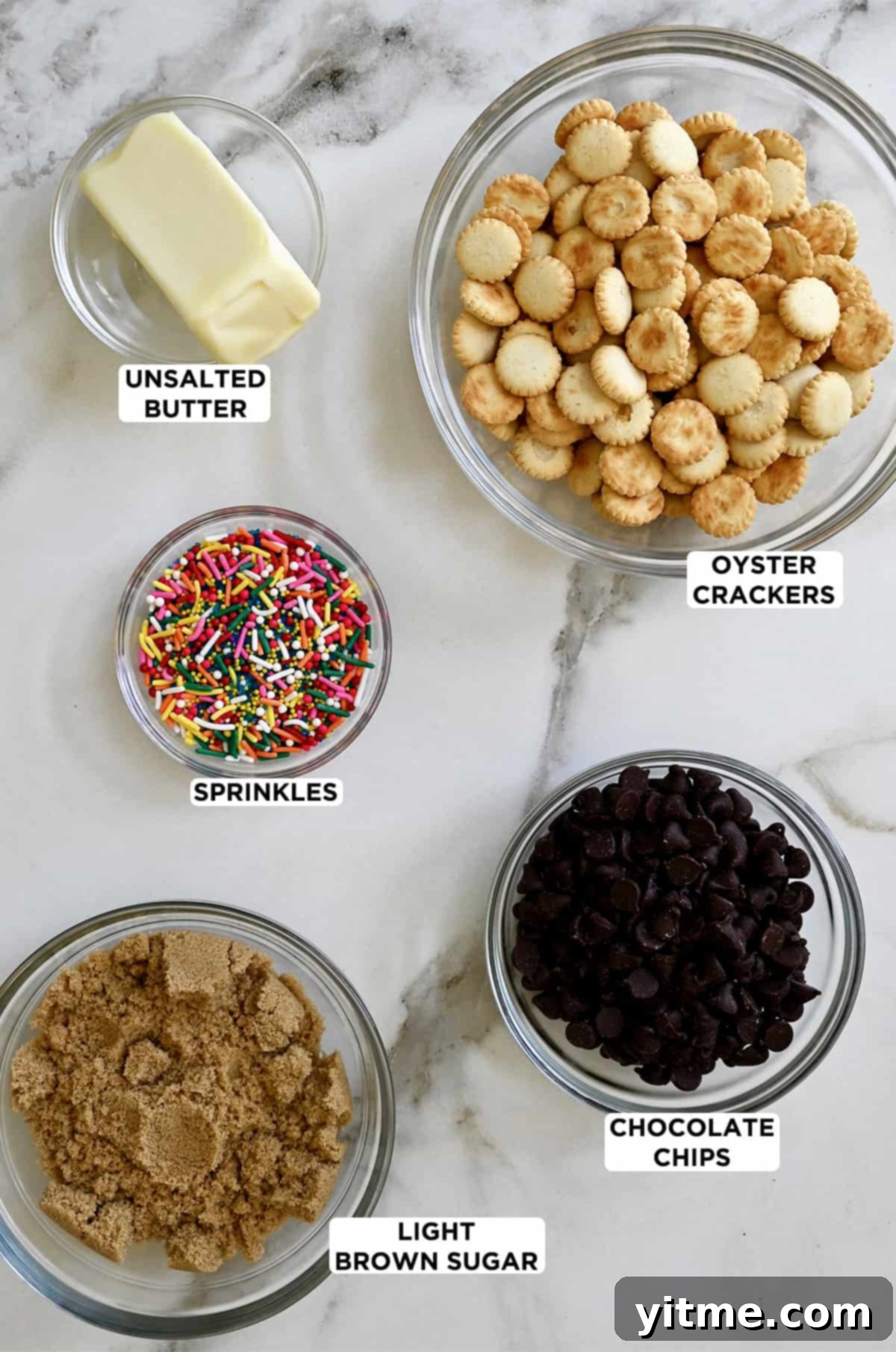 Five clear bowls containing oyster crackers, semisweet chocolate chips, brown sugar, sprinkles and butter.