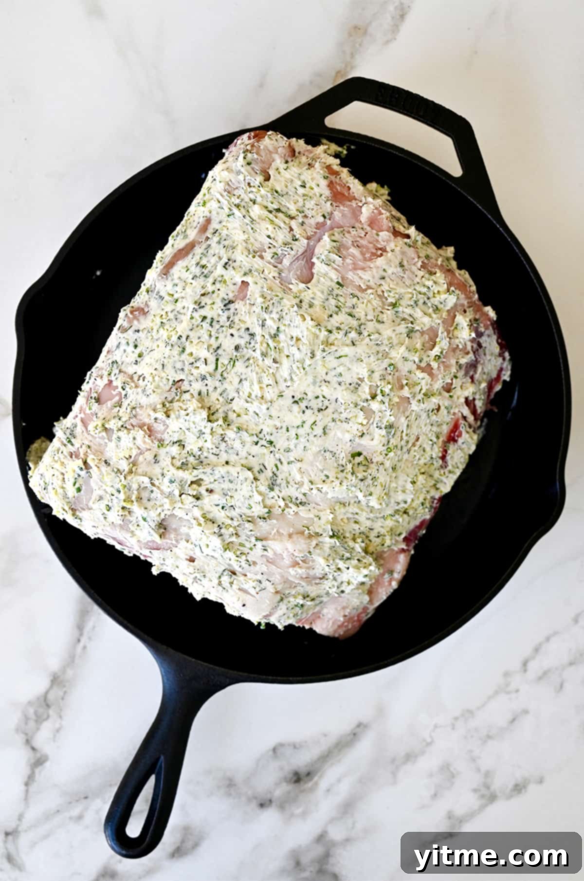 Prime rib roast coated in a garlic herb butter rub in a cast-iron skillet.