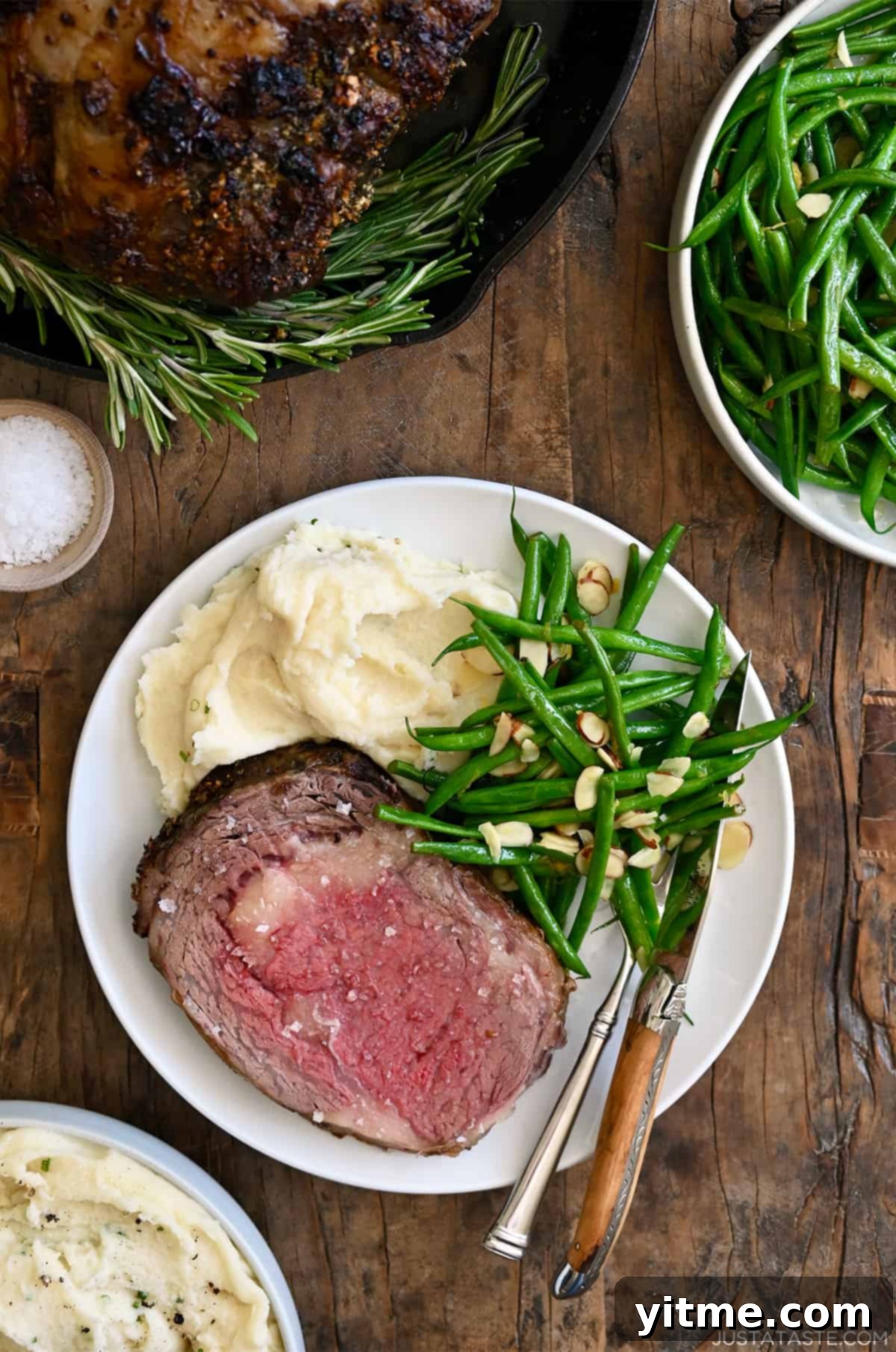 Prime rib cooked to medium-rare on a dinner plate with blistered green beans and mashed potatoes.
