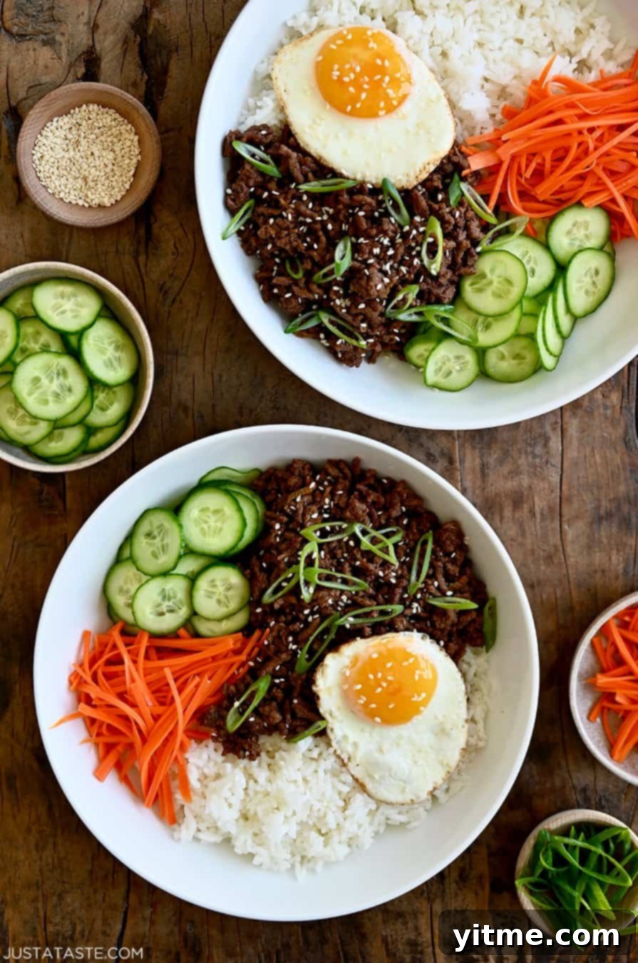 A top-down view of two colorful Korean Beef Bowls, each filled with seasoned ground beef, white rice, shredded carrots, sliced cucumber, and a perfectly fried egg.