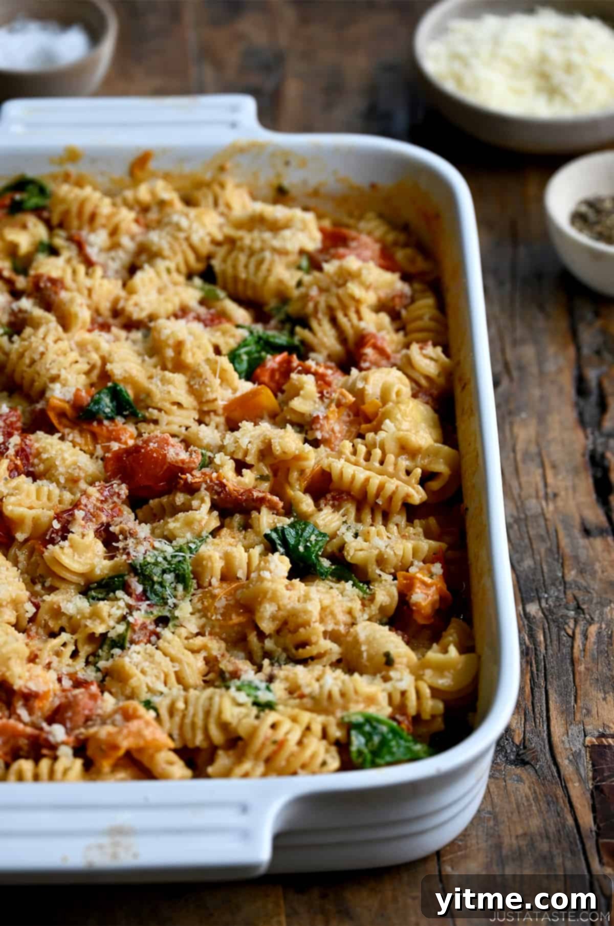 A white baking dish filled with creamy Baked Boursin Cheese Pasta with Sundried Tomatoes and Spinach, generously sprinkled with Parmesan cheese.