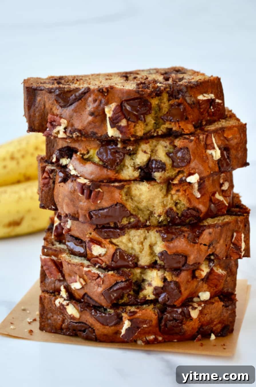 Moist slices of Greek Yogurt Banana Bread stacked on a plate with fresh bananas in the background, ready to be enjoyed.